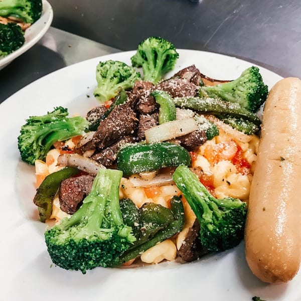 Steak and broccoli with peppers, onions, and macaroni and cheese, served with a breadstick.