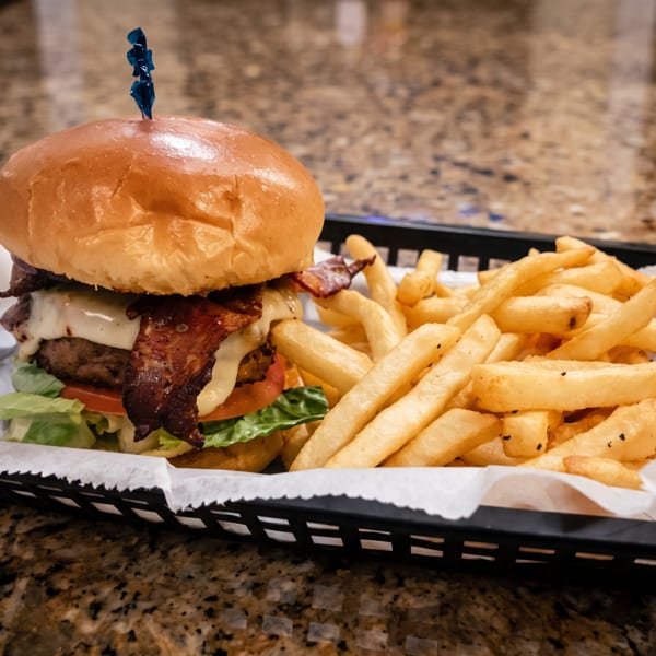 A juicy bacon cheeseburger with lettuce and tomato, served with golden french fries in a basket.