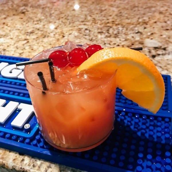 A vibrant orange cocktail with ice, cherries, and an orange slice on a blue bar mat.